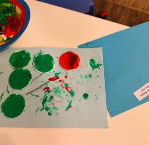 Gebasteltes Bild einer kleinen Raupe Nimmersatt aus bemalten Papierkreisen auf blauem Papier, gestaltet von einem Kind der Großtagespflege Rappelkiste Hochdahl.